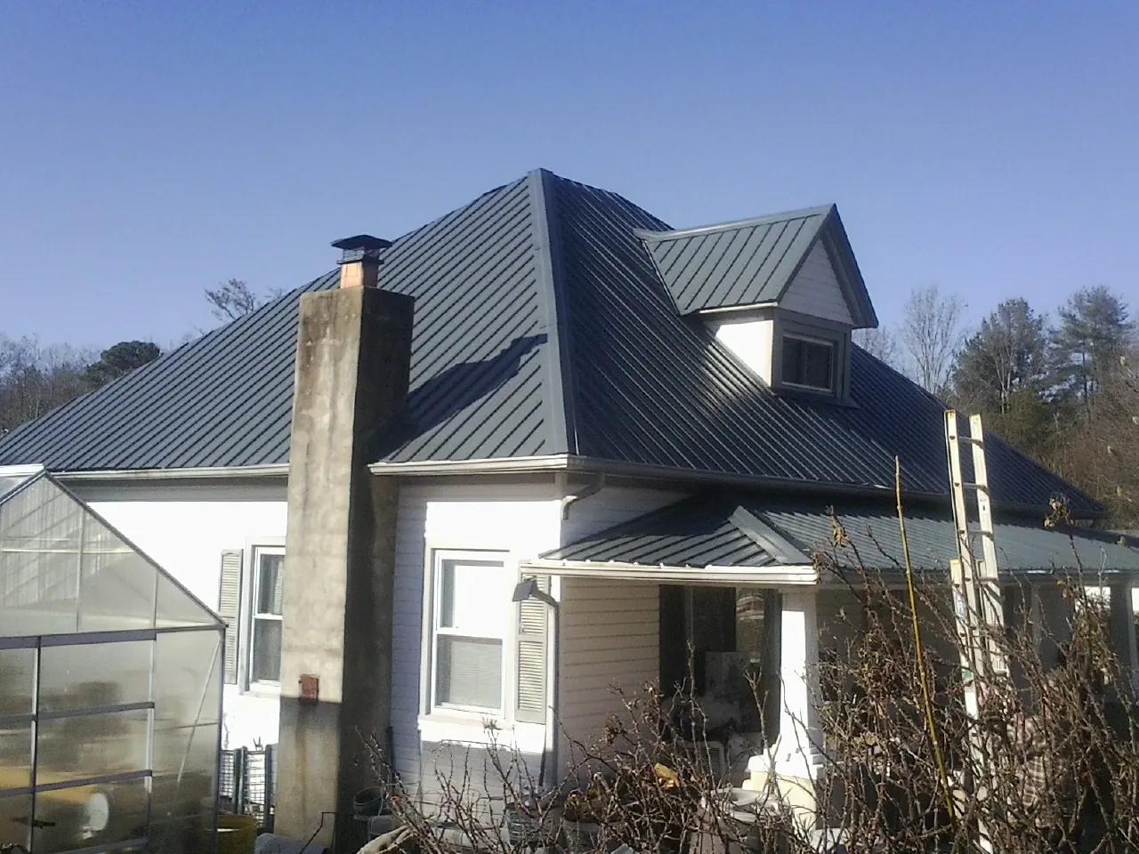 Dark blue standing seam metal roof on a white farmhouse with dormer — Slate & Tile Roof Repair by Roofing Brothers in Velva