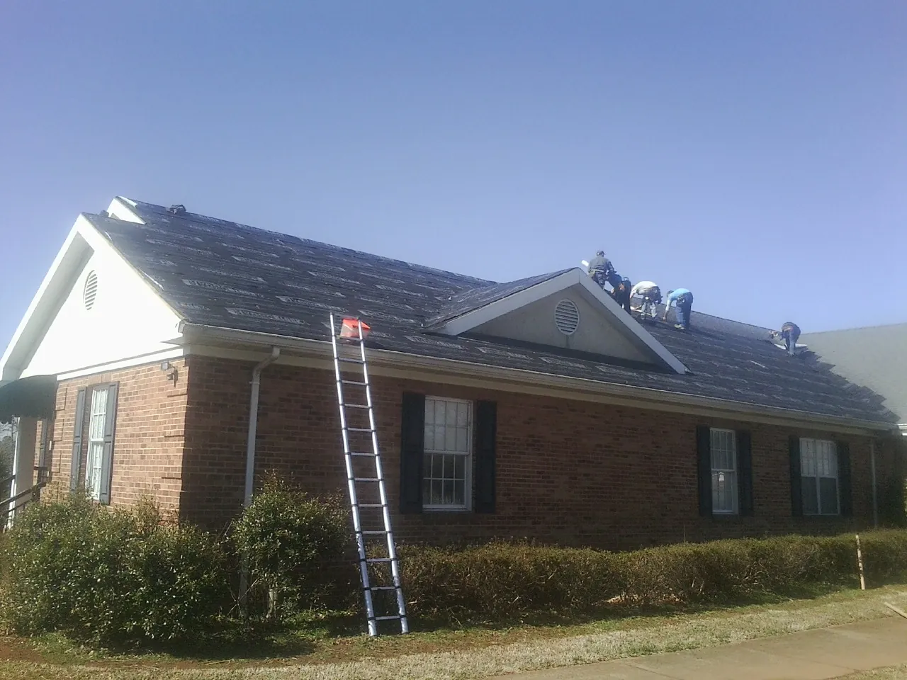 Crew tearing shingles off a brick ranch roof with a ladder set — Metal Roof Repair work by our crew in Velva