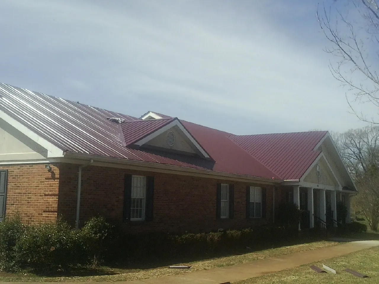 Red metal roof with gabled entries on a long brick building, from a Hail Damage Roof Repair job in Velva