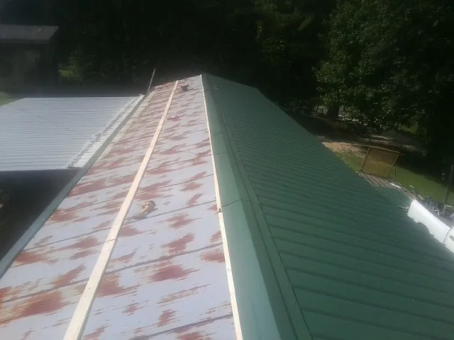 Old rusted panels beside newly installed green metal roofing — Wind Damage Roof Repair by Roofing Brothers in Velva