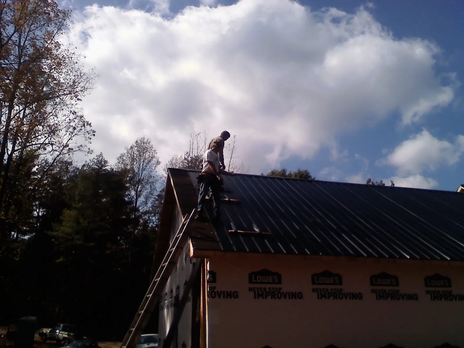 Roofer fastening dark metal panels high against a cloudy sky, from a Roof Inspection job in Velva