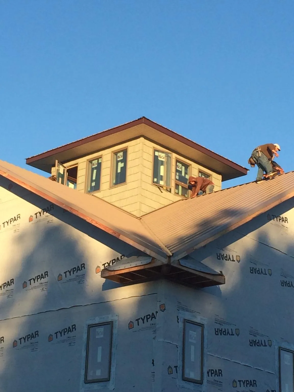 Roofers working around a rooftop cupola on a new metal roof at sunset — Roof Waterproofing in Velva by Roofing Brothers